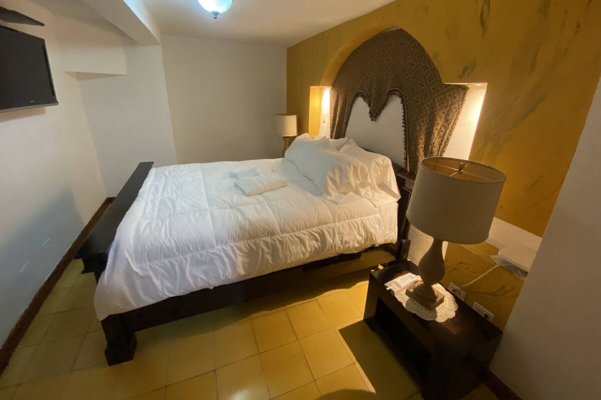 A hotel room with a bed, bedside lamp, and a decorative headboard.