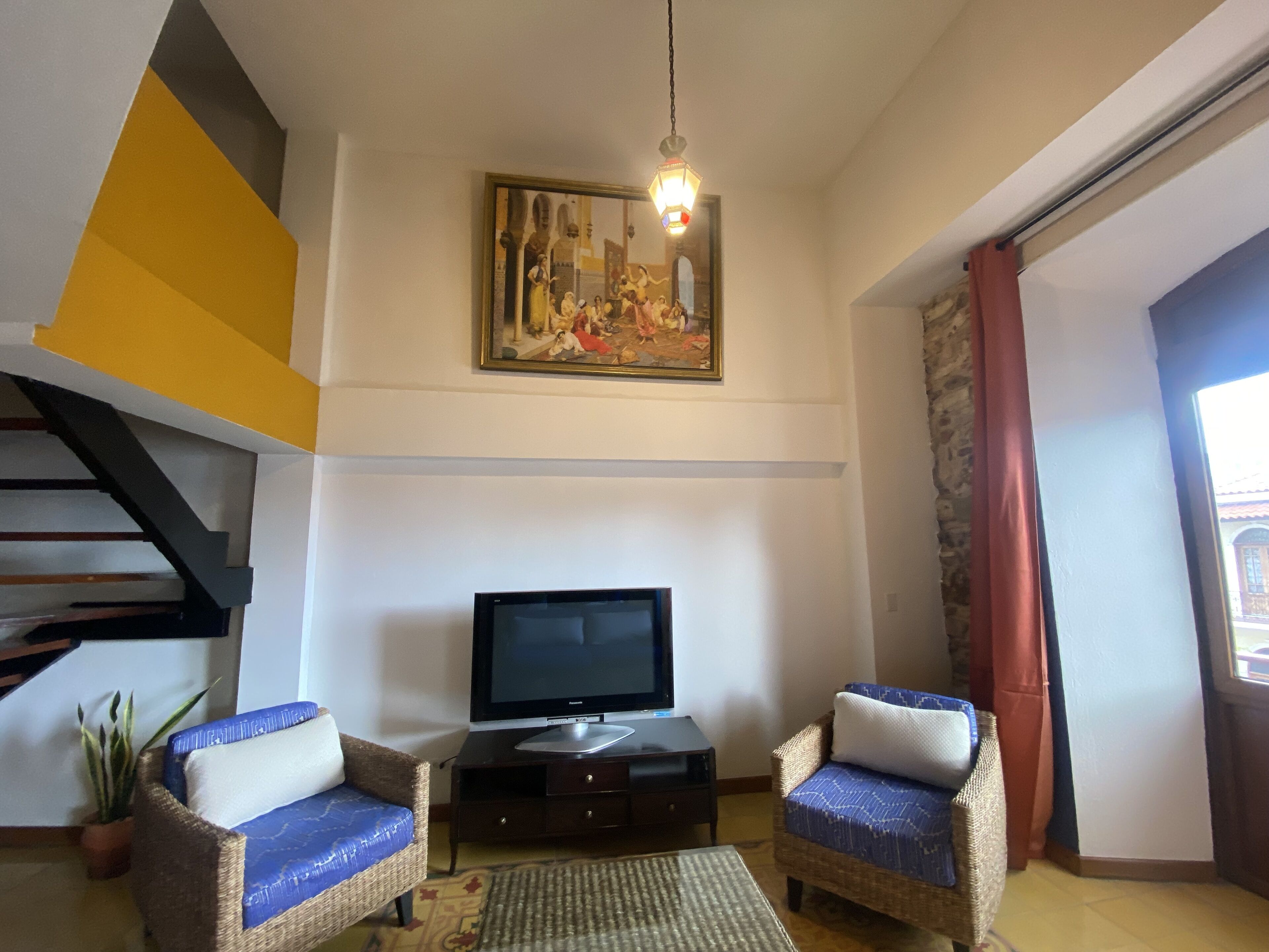 Una sala de estar con dos sofás de mimbre, un televisor de pantalla plana, un cuadro y una escalera.
