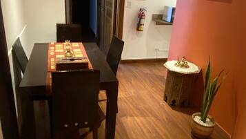 Un coin repas avec une table et des chaises en bois, une petite table d’appoint agrémentée d’un objet décoratif, une plante en pot et un extincteur fixé au mur.
