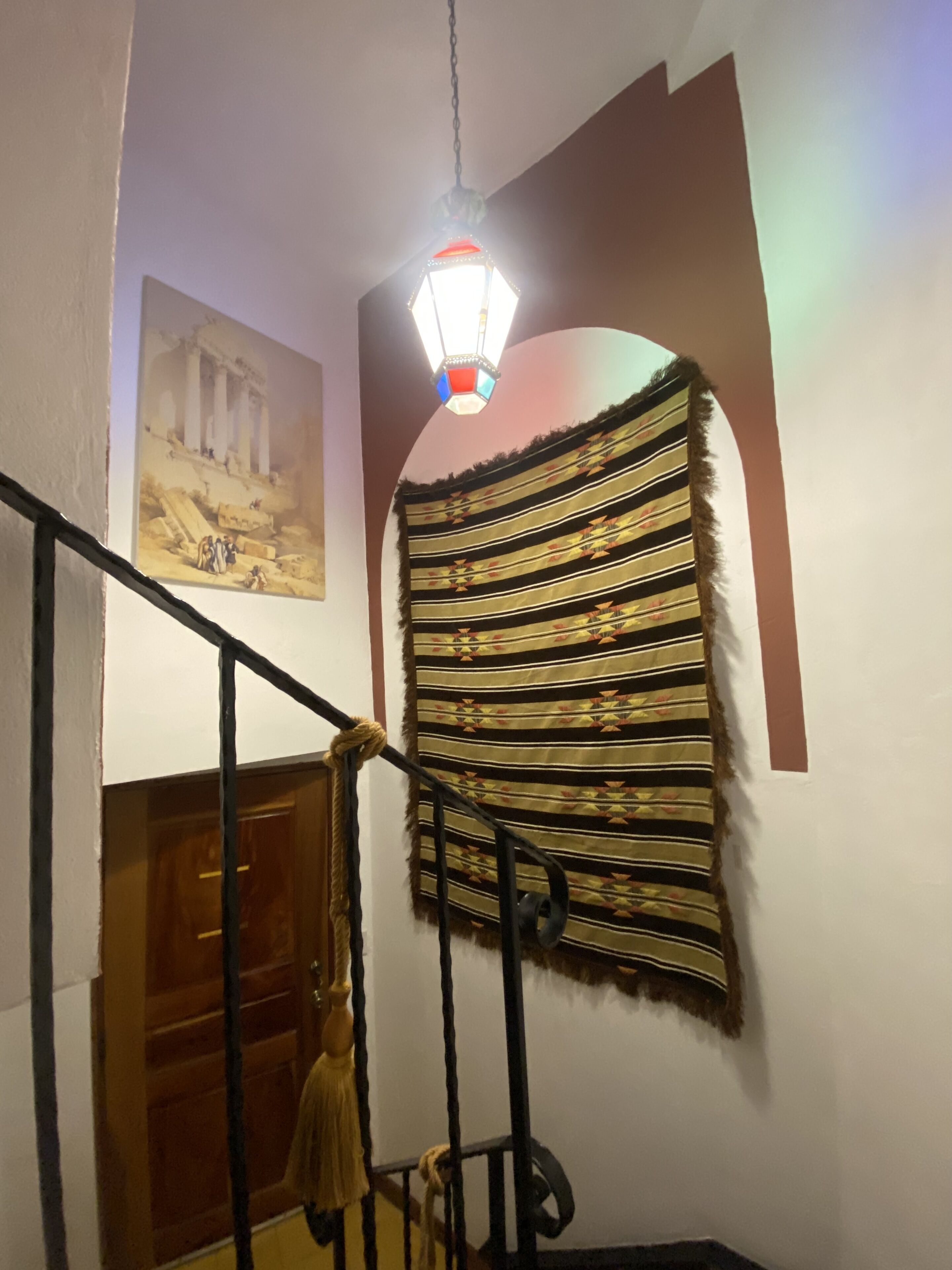 A staircase with a handrail, a wall-mounted tapestry, and a ceiling light fixture.