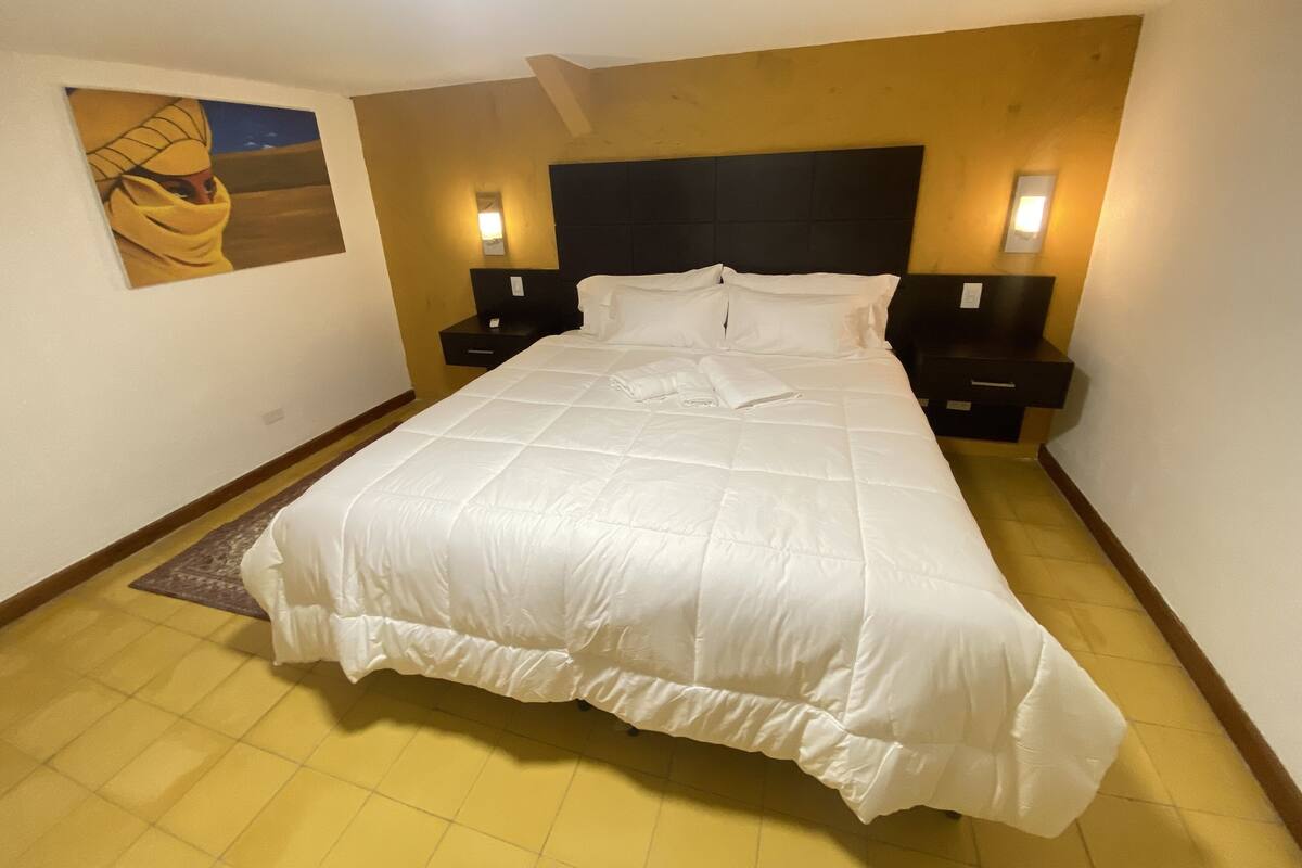 A hotel room with a large bed, two bedside tables, a headboard, and a painting on the wall.