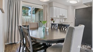 A dining area with a round table, chairs, a vase with a plant, and a view through a sliding door to a balcony. - Kinney #1 xxxxxxxxxx (Austin)