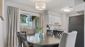 A dining area with a round table, chairs, a vase with a plant, and a view through a sliding door to a balcony. - Kinney #1 xxxxxxxxxx (Austin)