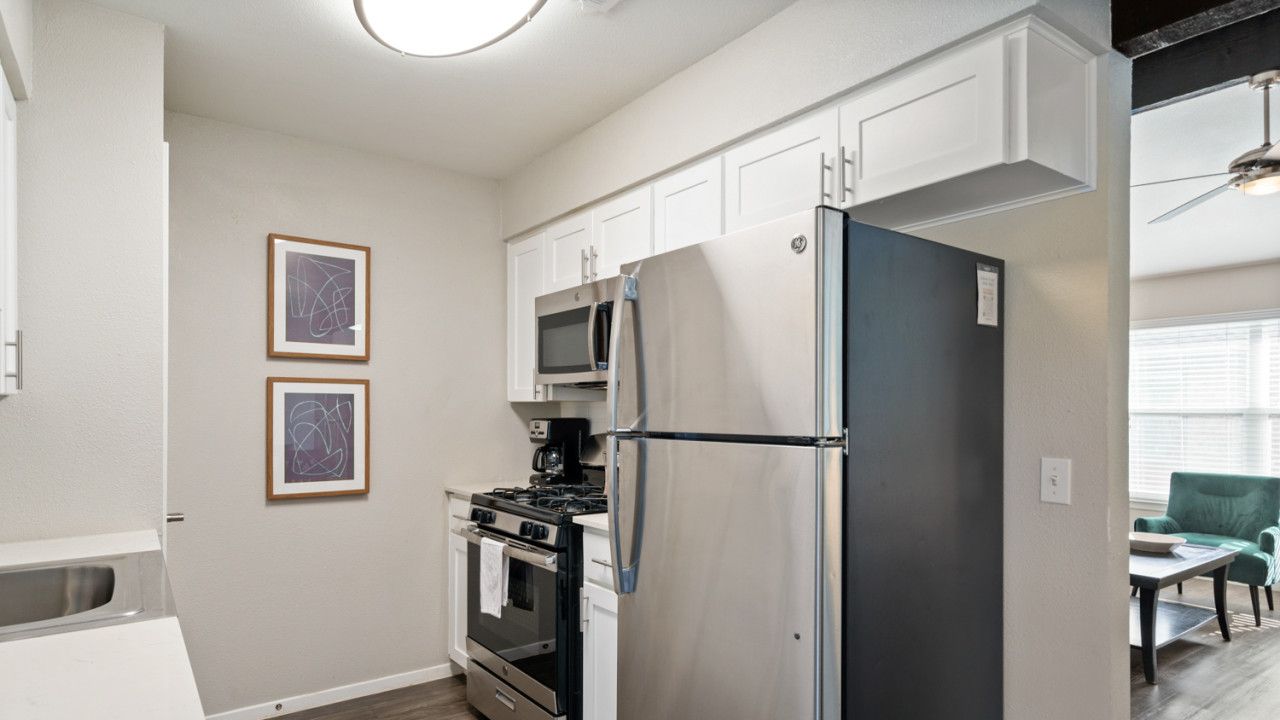 A modern kitchen with stainless steel appliances, white cabinetry, and a dining area with a green chair.