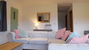 A living room with a light-colored sectional sofa, a wooden coffee table, a mirror, and a lamp on a side table. - Red Kite Lodge - UK32610 (Stanner, near Kington)