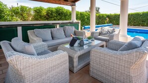 A covered outdoor seating area with wicker furniture, a glass table, and a pool in the background. - Casa Josephine by Portucasa (Olhao)