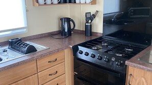 A compact kitchen with wooden cabinets, a stove, oven, and a sink. - Stunning 2 Bedroom Static Caravan set in 60 Acres (Lincoln)