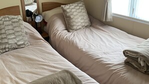 A bedroom with two beds, a mirror, a nightstand, and a window with curtains. - Stunning 2 Bedroom Static Caravan set in 60 Acres (Lincoln)