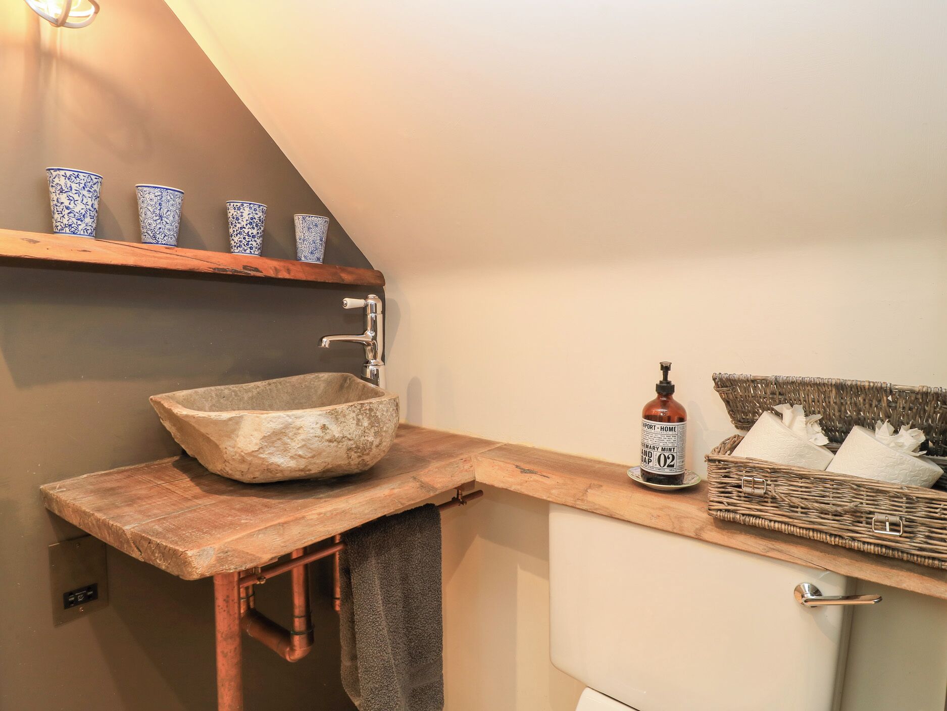 A rustic bathroom with a stone sink, wooden shelves, and a wicker basket.
