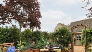 A garden with a wooden bench, a table with chairs, and a pergola. - Pudding Hill Barn Cottage (Cirencester)