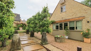A stone pathway leading to a stone building with a window and a door. - Pudding Hill Barn Cottage (Cirencester)