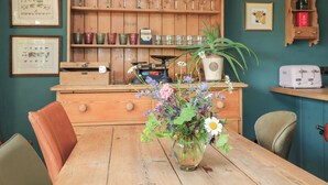 A rustic kitchen with wooden cabinets, a vintage radio, and a floral centerpiece on the table. - Pudding Hill Barn Cottage (Cirencester)