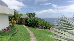 A pathway leading to a gazebo surrounded by tropical vegetation, overlooking a coastal view. - Uplifting 3 bed beach island cottage (cap estate)