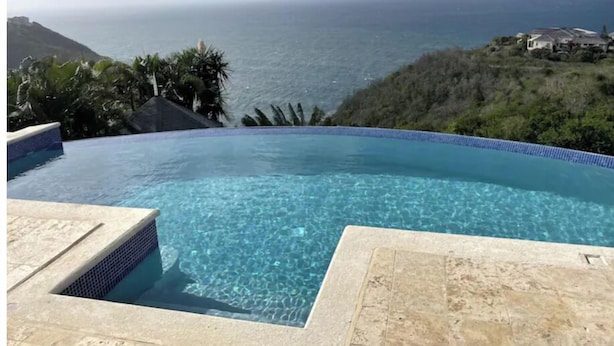 A clear blue infinity pool with a view of the ocean and a mountainous landscape. - Uplifting 3 bed beach island cottage (cap estate)