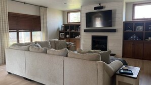 Un salon comprenant un canapé d’angle, une cheminée, un téléviseur à écran plat et un meuble en bois.