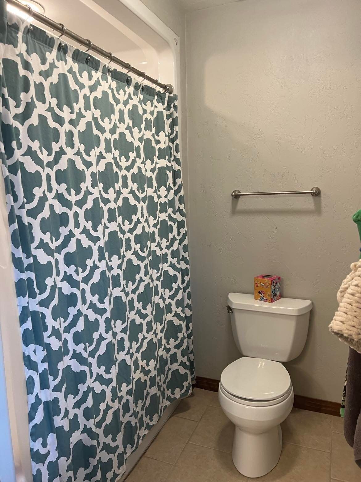 Une salle de bain avec un rideau de douche à motifs, des toilettes et un porte-serviettes.