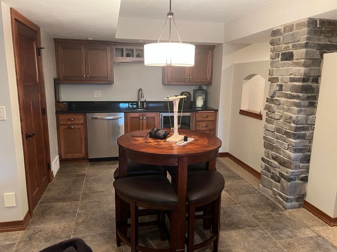 Una cocina con armarios de madera, una mesa redonda con dos sillas, una pared de acento de piedra y una lámpara colgante.