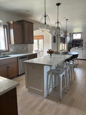 A modern kitchen with wooden cabinets, a white island with bar stools, pendant lighting, and a view of the outdoors. - Beautiful home Sleeps 10 with Heated Inground Pool (Neenah)
