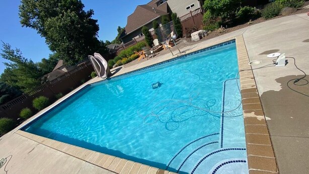 Una piscina rectangular con agua azul cristalina, rodeada por un suelo de ladrillo y un paseo de hormigón.