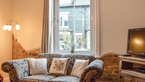 A living room with a patterned sofa, a television, and a window with a view of buildings. - 2 bedroom accommodation in Keswick (Keswick)