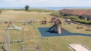 A playground with various play structures, a picnic area, and a building with a red-tiled roof.