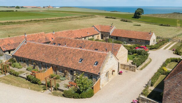 A rural property with stone buildings, a gravel driveway, and a view of the sea.