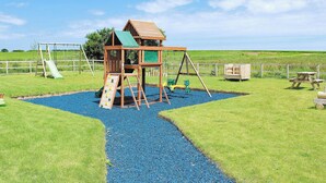 A playground with a wooden playhouse, slides, swings, and a picnic table.