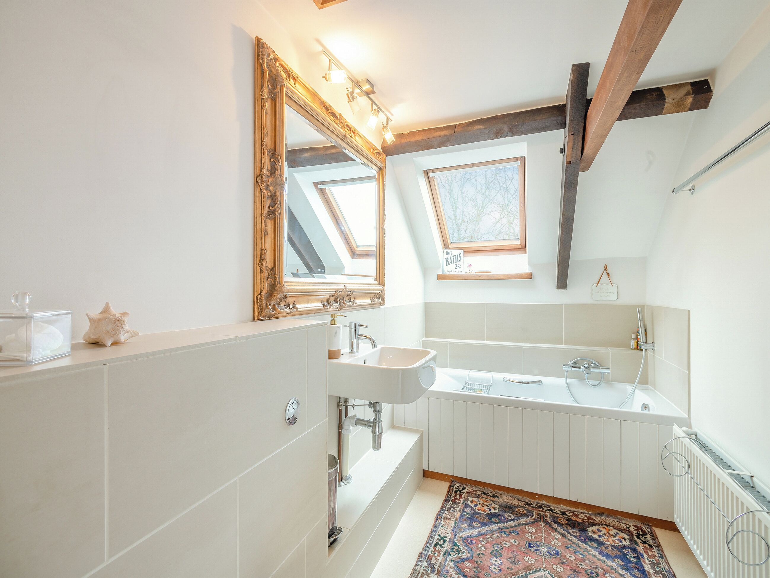 Een moderne badkamer met dakraam, grote spiegel, badkuip en wastafel.