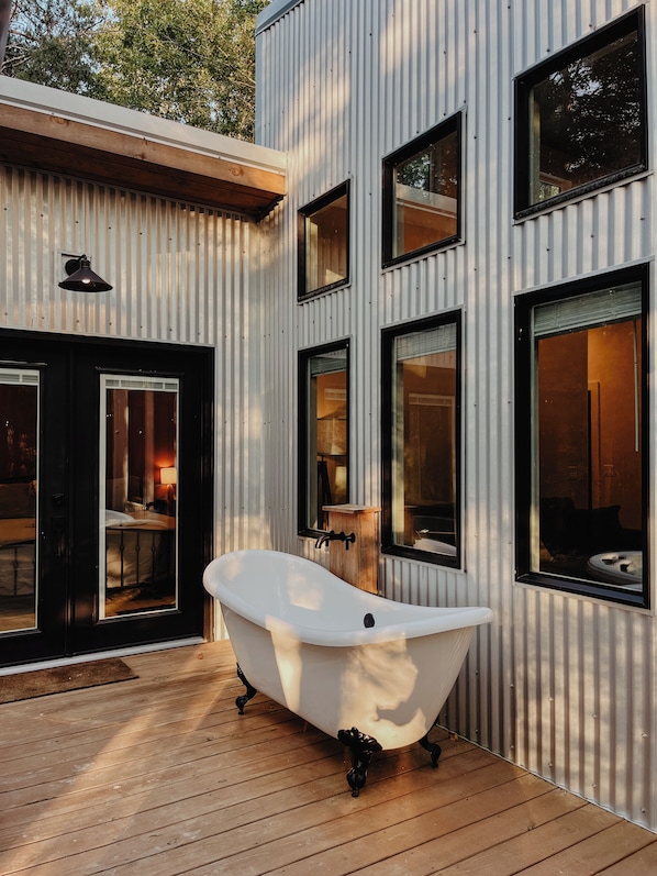A modern building with a large bathtub on a wooden deck, multiple windows, and a door leading to a room.