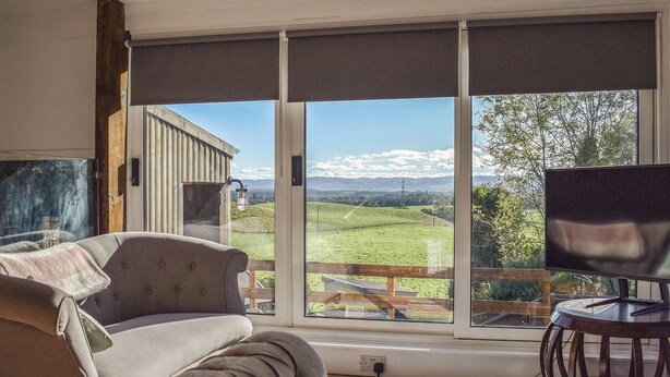 A room with a large sliding glass door leading to a scenic outdoor view, a sofa, a small table, and a television. - 2 bedroom accommodation in Crieff (Crieff)