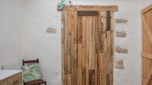 A room with a rustic wooden door, a small chair, and a bed with a floral bedspread. - 2 bedroom accommodation in Crieff (Crieff)