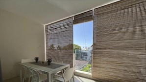 Een balkon met een eettafel en stoelen, afgedekt met horizontale zonwering, met uitzicht op een woonwijk.