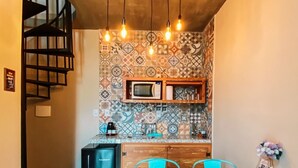 Uma cozinha compacta com mesa de madeira e cadeiras cor turquesa, micro-ondas e painel de fundo padronizado.