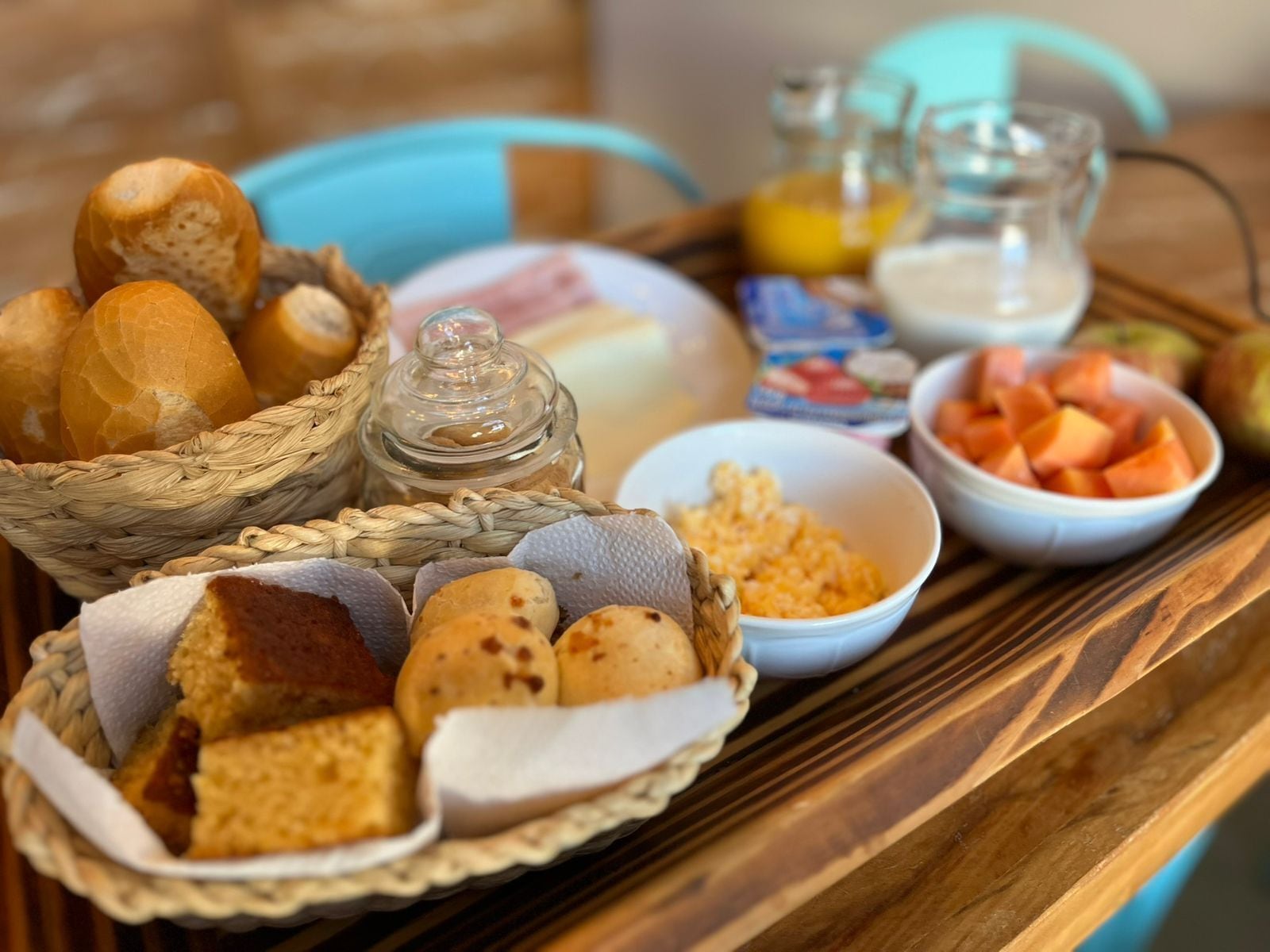 A breakfast tray with bread, pastries, scrambled eggs, fruit, and beverages.