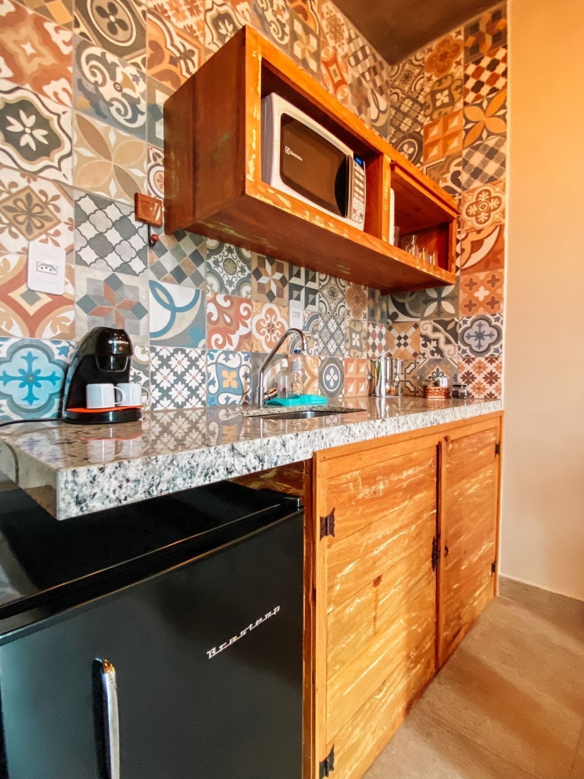 Una cocina con salpicadero estampado, microondas, cafetera y armarios de madera.