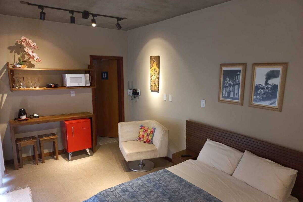 A bedroom with a bed, a desk with a red cabinet, a chair, a microwave, and a small table with a vase of flowers.