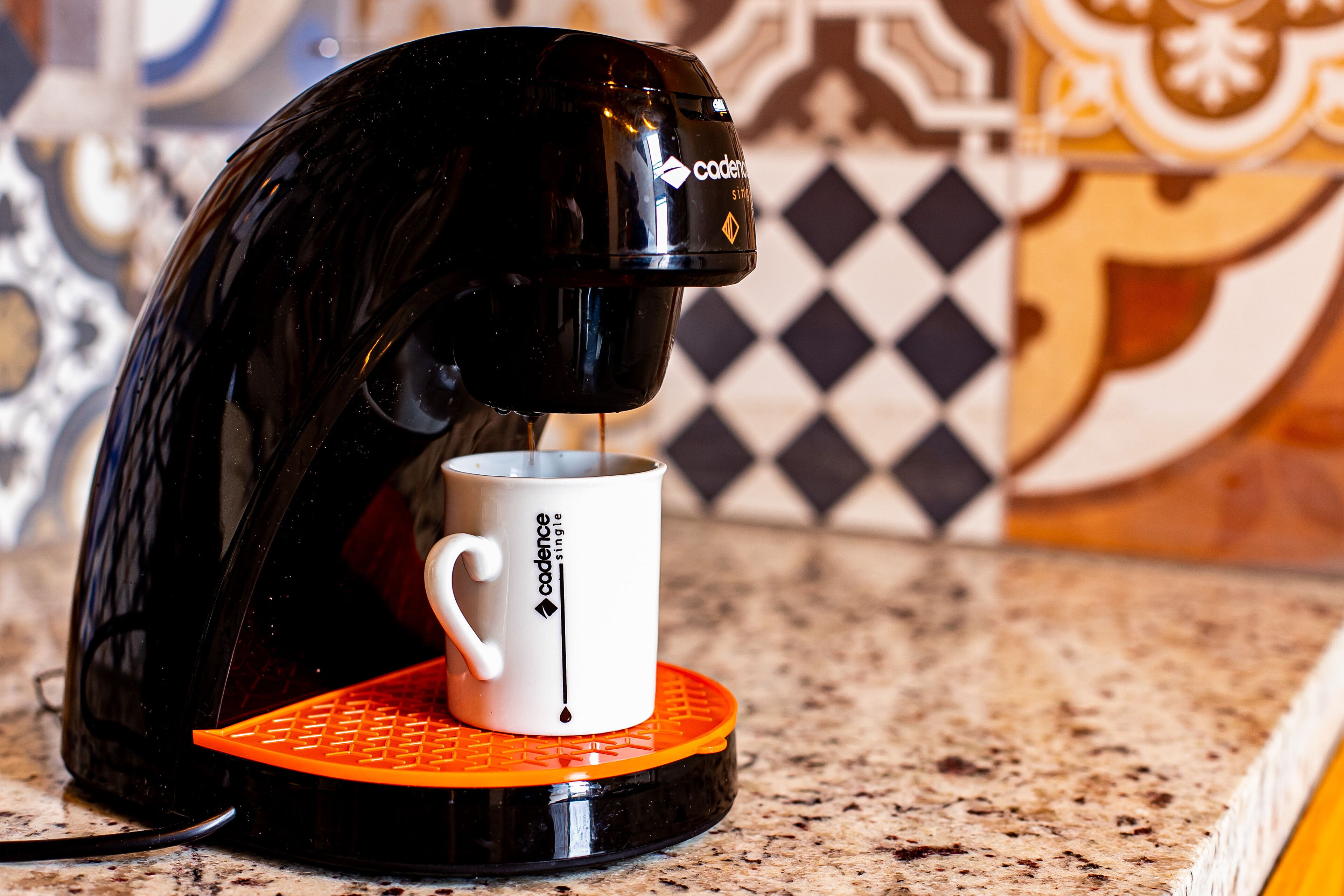 A coffee maker with a white mug on an orange coaster.