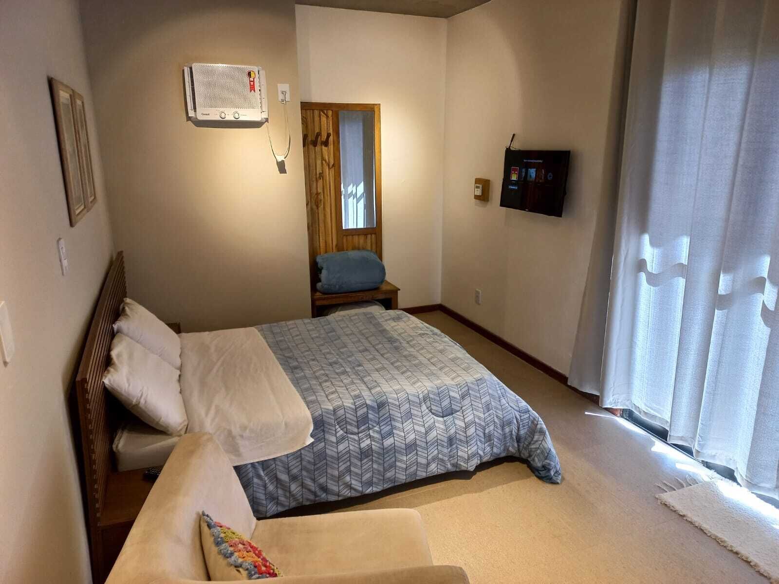 A bedroom with a bed, a bedside table, a TV, and a window with curtains.
