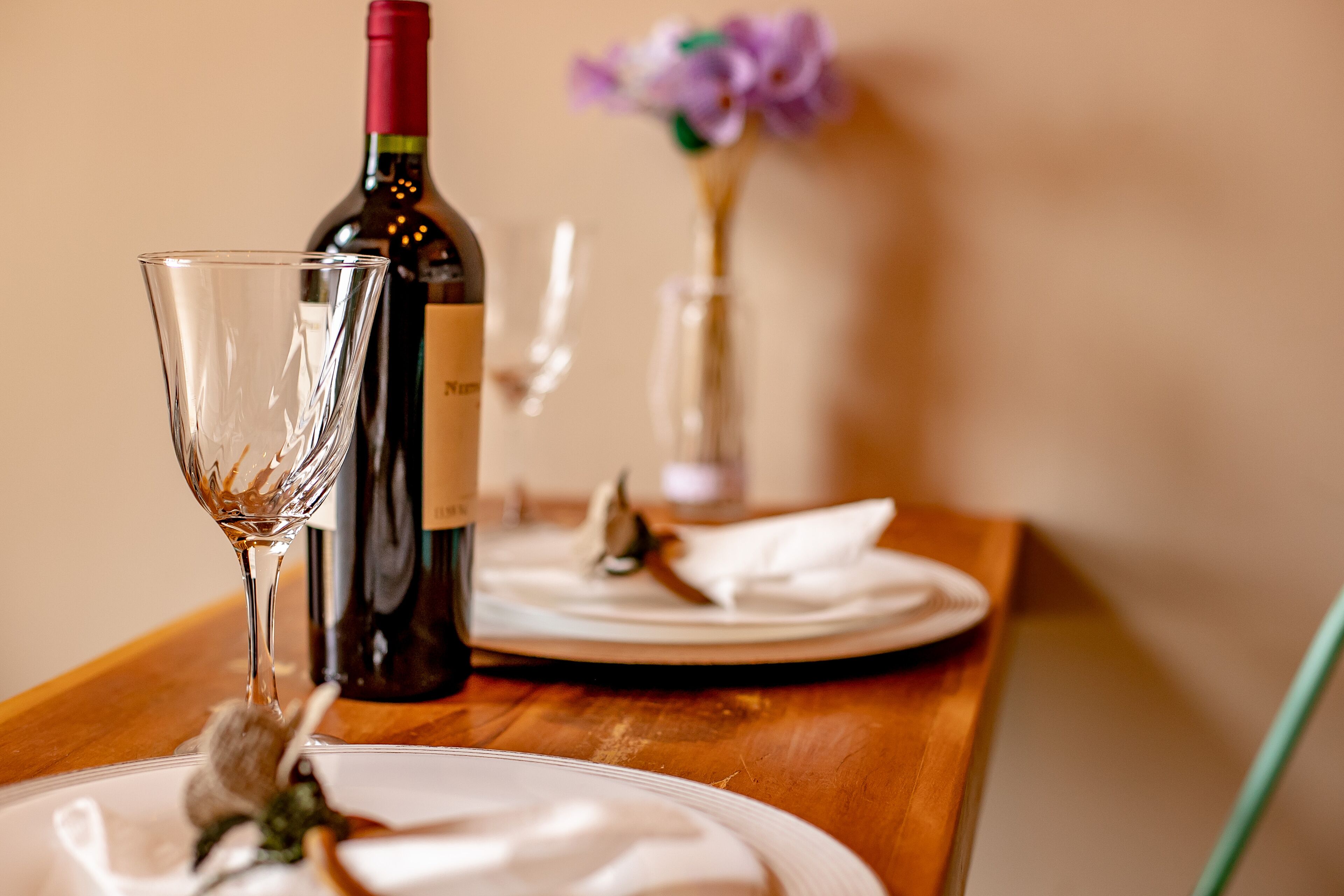 A dining table with a wine bottle, a glass, and a plate with a napkin.