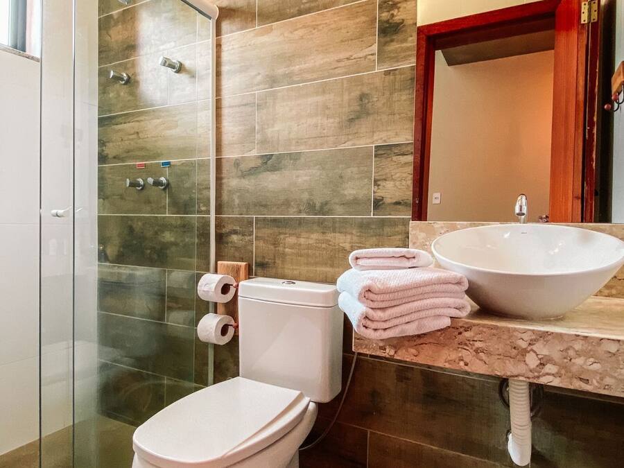 A modern bathroom with a glass shower enclosure, a white toilet, a sink with a large basin, and a mirror with a wooden frame.
