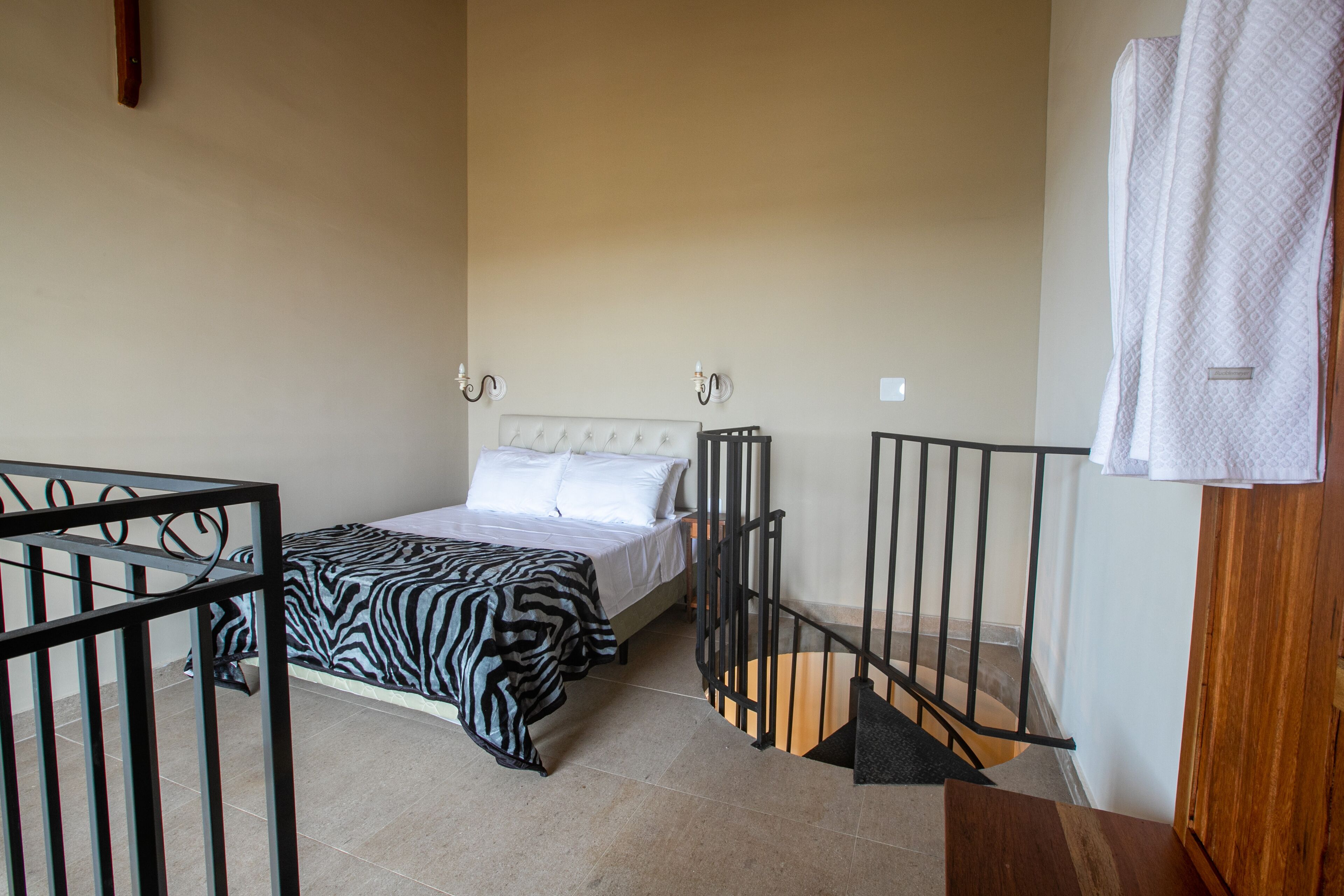 Quarto com cama, manta estampada de zebra, cabeceira de madeira e escada com corrimão.