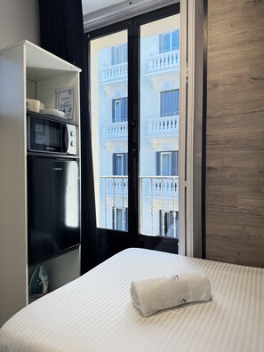 Une chambre d’hôtel équipée d’un lit, d’un four à micro-ondes, d’un fer à repasser et offrant une vue sur un immeuble doté de balcons.