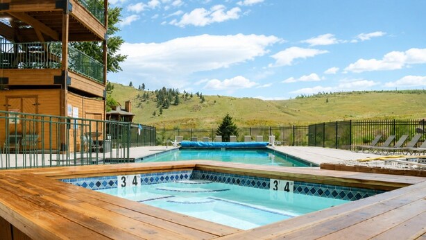 A rectangular pool with a wooden deck surrounding it, set against a backdrop of a hilly landscape. - Ski In Ski Out Condo in Granby (Granby)
