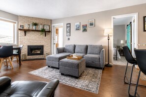 Ein Wohnzimmer mit Kamin, grauem Sofa, Ottoman und Couchtisch.