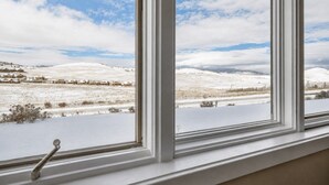 A window with a view of a snow-covered landscape, including houses and distant hills. - Ski In Ski Out Condo in Granby (Granby)
