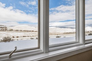 Ein Fenster mit Blick auf eine schneebedeckte Landschaft, einschließlich Häuser und ferne Hügel.