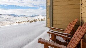 A wooden deck with two chairs, overlooking a snowy landscape with distant mountains. - Ski In Ski Out Condo in Granby (Granby)