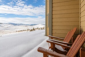 Eine Holzterrasse mit zwei Stühlen, mit Blick auf eine verschneite Landschaft und ferne Berge.