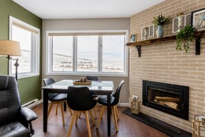 Ein Essbereich mit Tisch und Stühlen, einem Kamin und Blick auf eine verschneite Landschaft durch große Fenster.