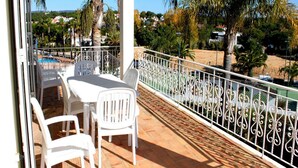 Ein Balkon mit weißen Stühlen und einem Tisch, mit Blick auf einen Pool und Palmen.